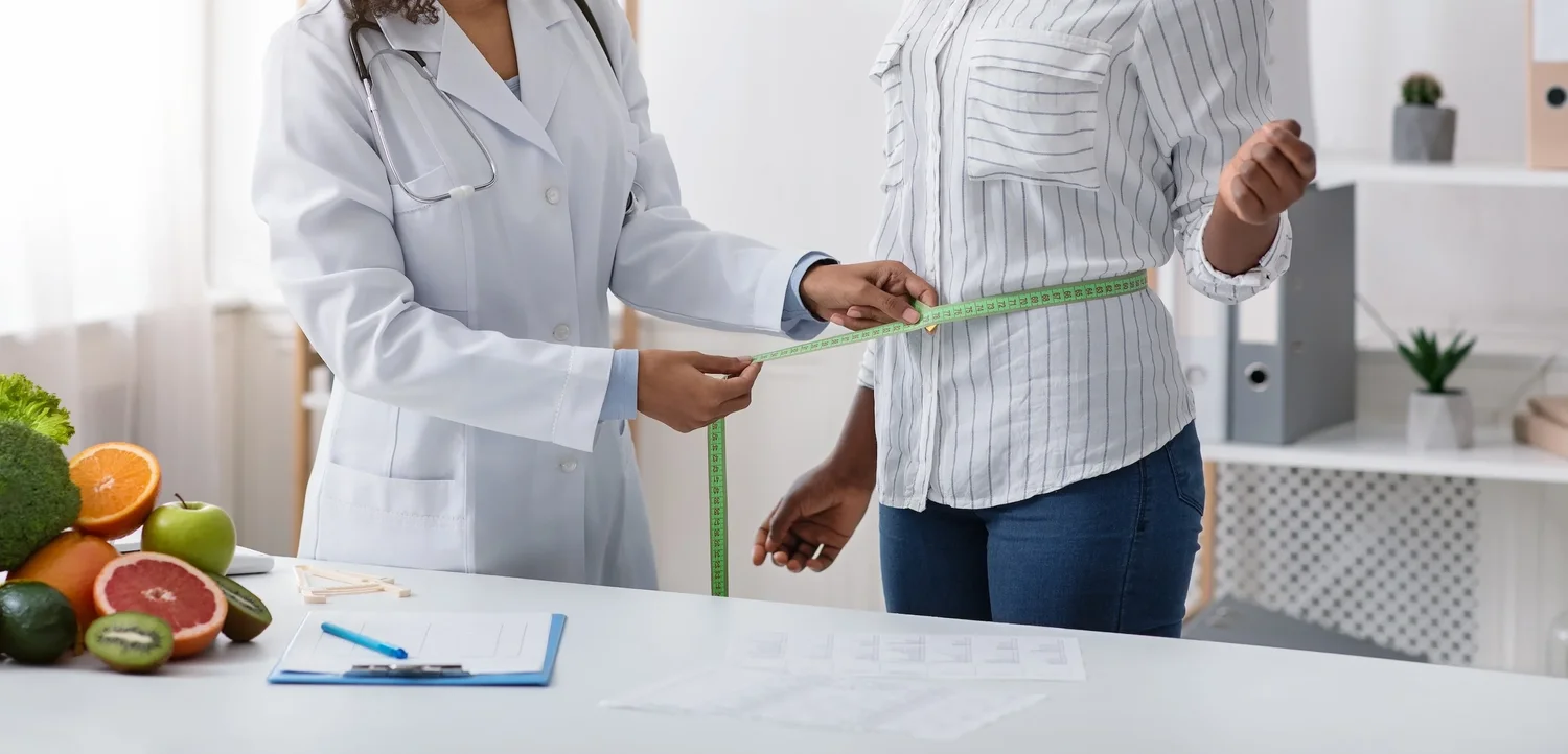 Clinician measuring a patient's waist in a consulting room